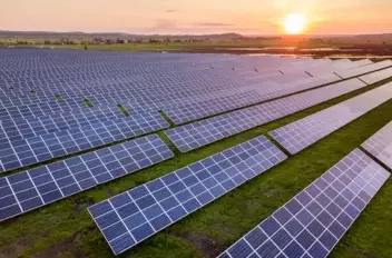 Large solar farm in agricultural land generating renewable energy at sunset.