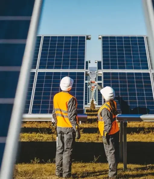 Two solar engineers in safety gear inspecting large solar panel installation outdoors.